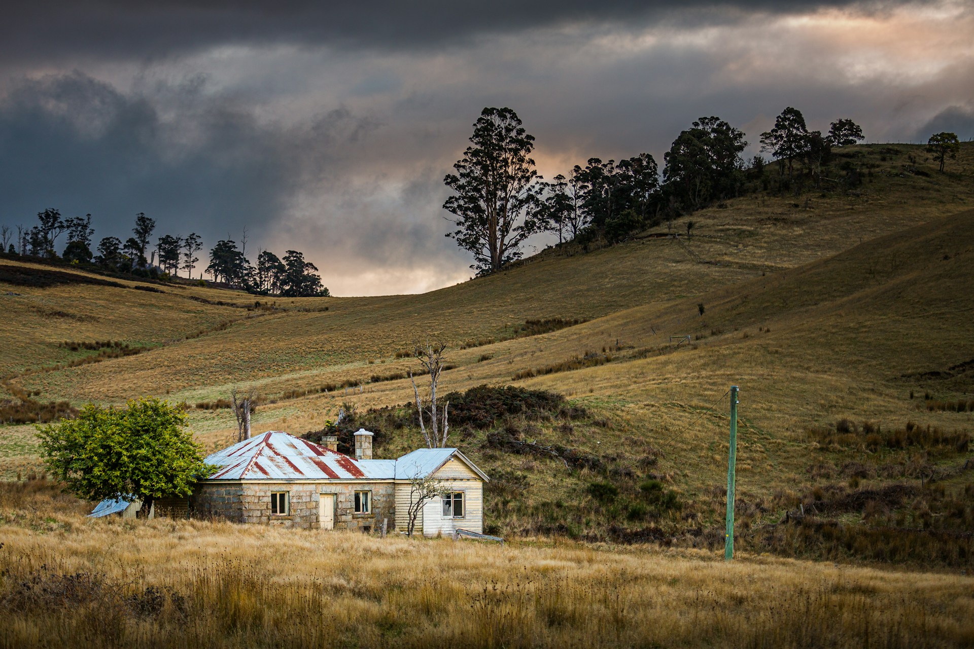 White and brown brick cottage nestled in rolling green hills under a stormy sky